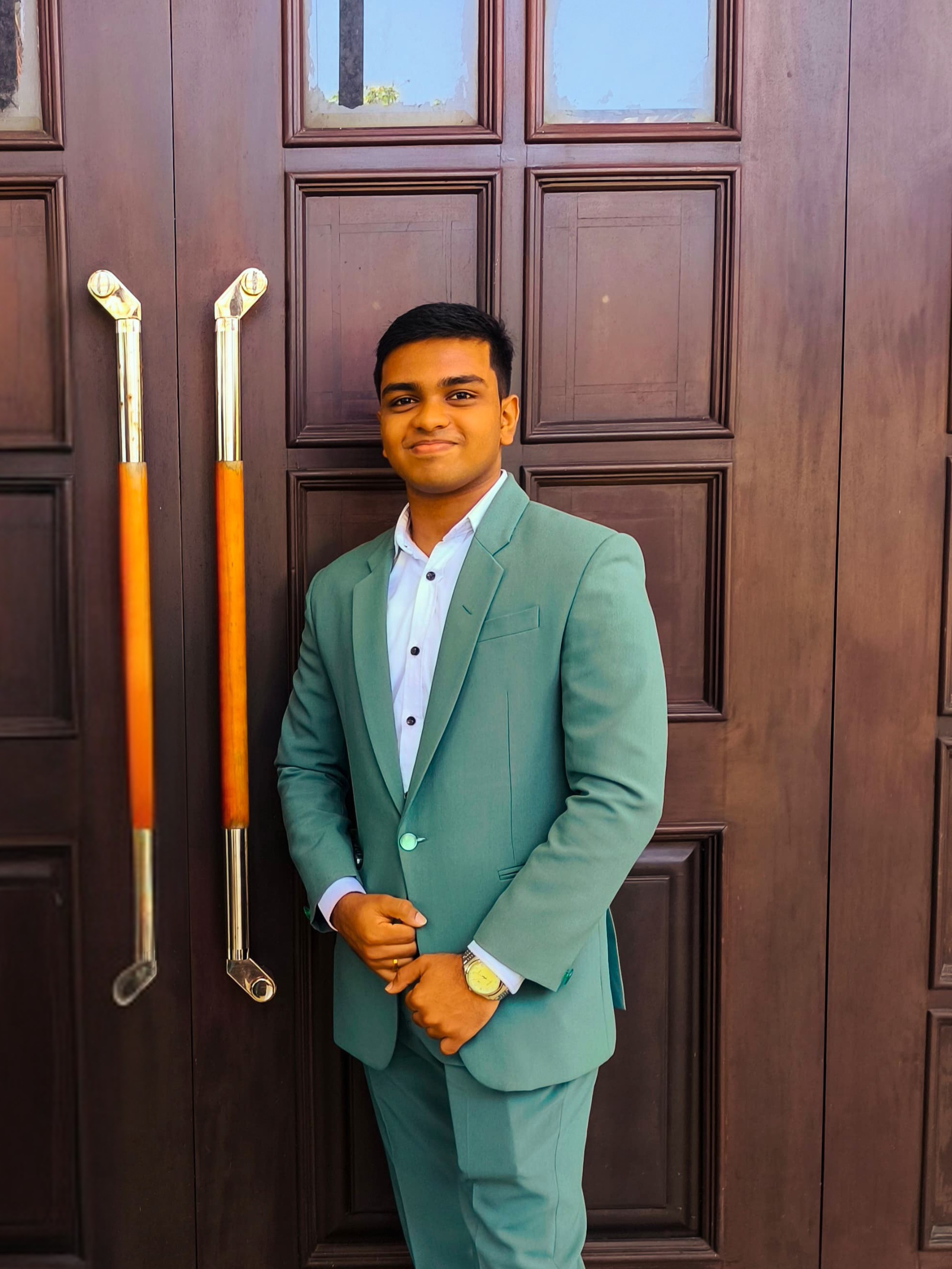 Tharindu Sandaruwan wearing a teal suit in front of a wooden door.