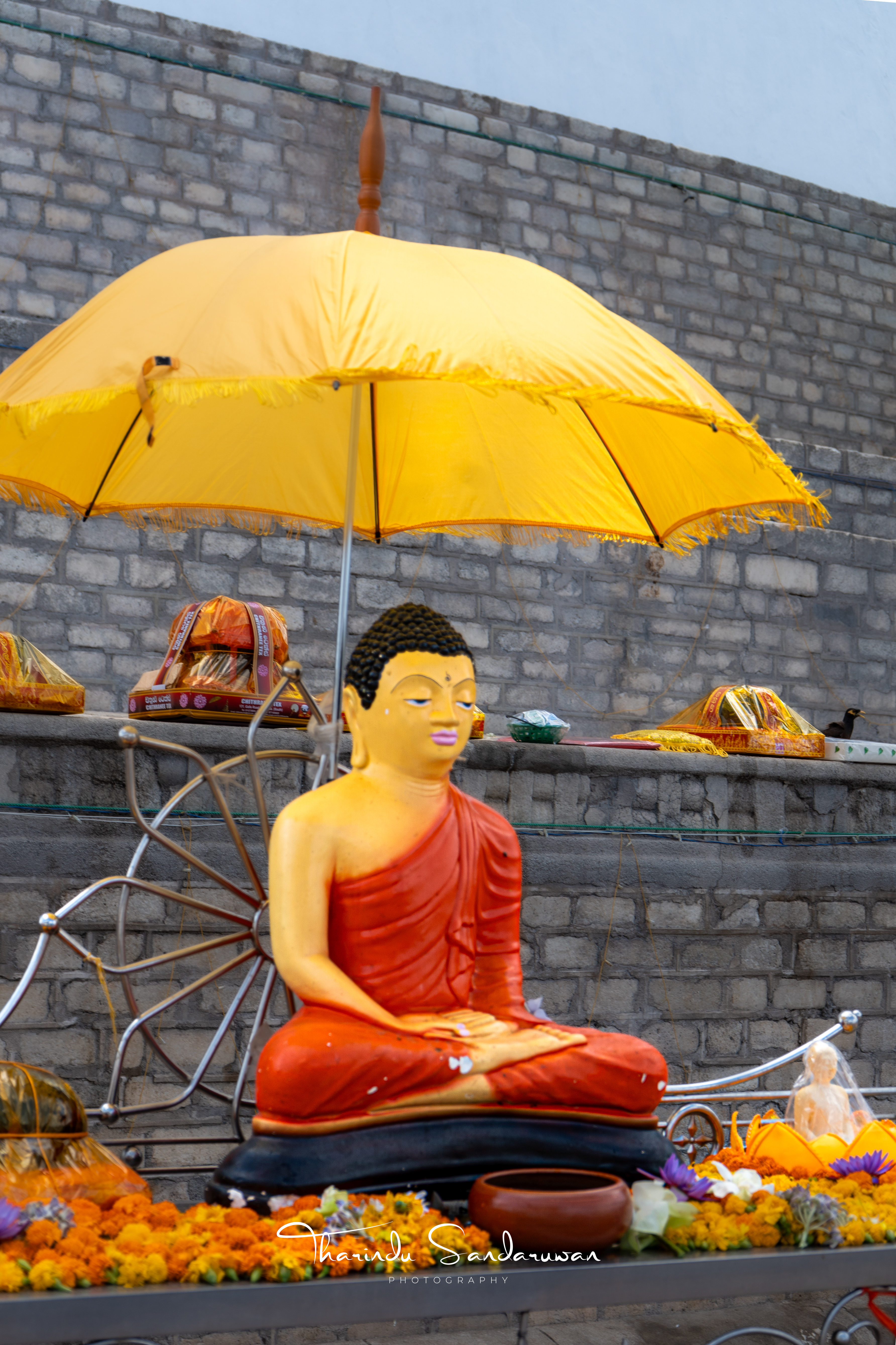 A seated Buddha statue and offerings beneath a bright yellow parasol.