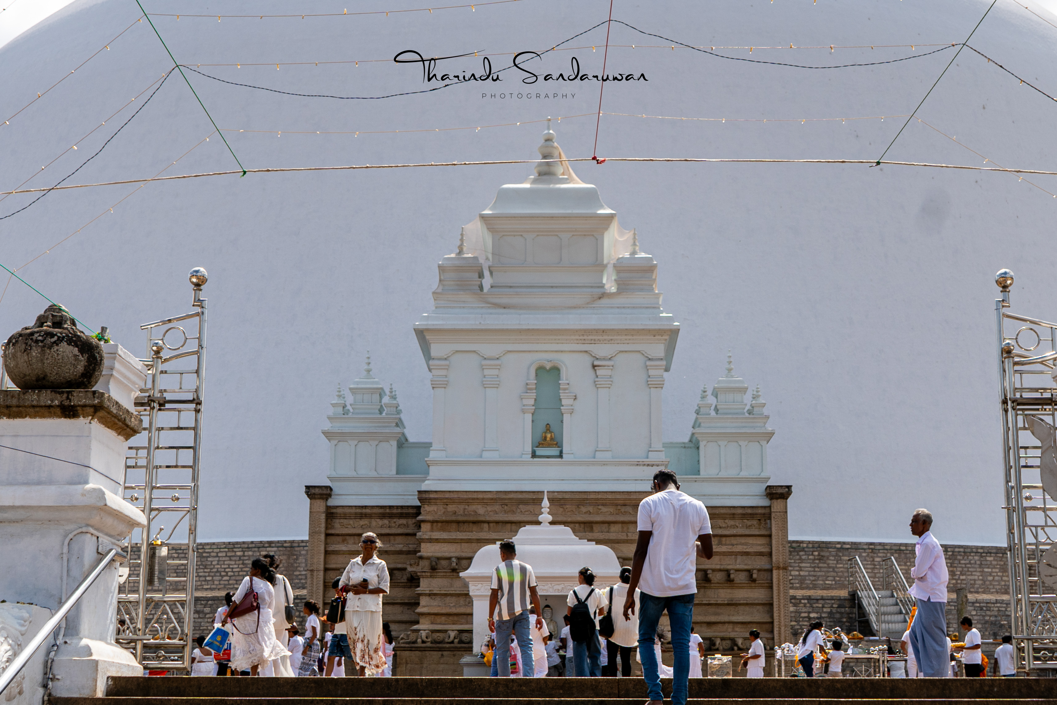 Visitors approach a shrine in front of a large white stupa in Anuradhapura.