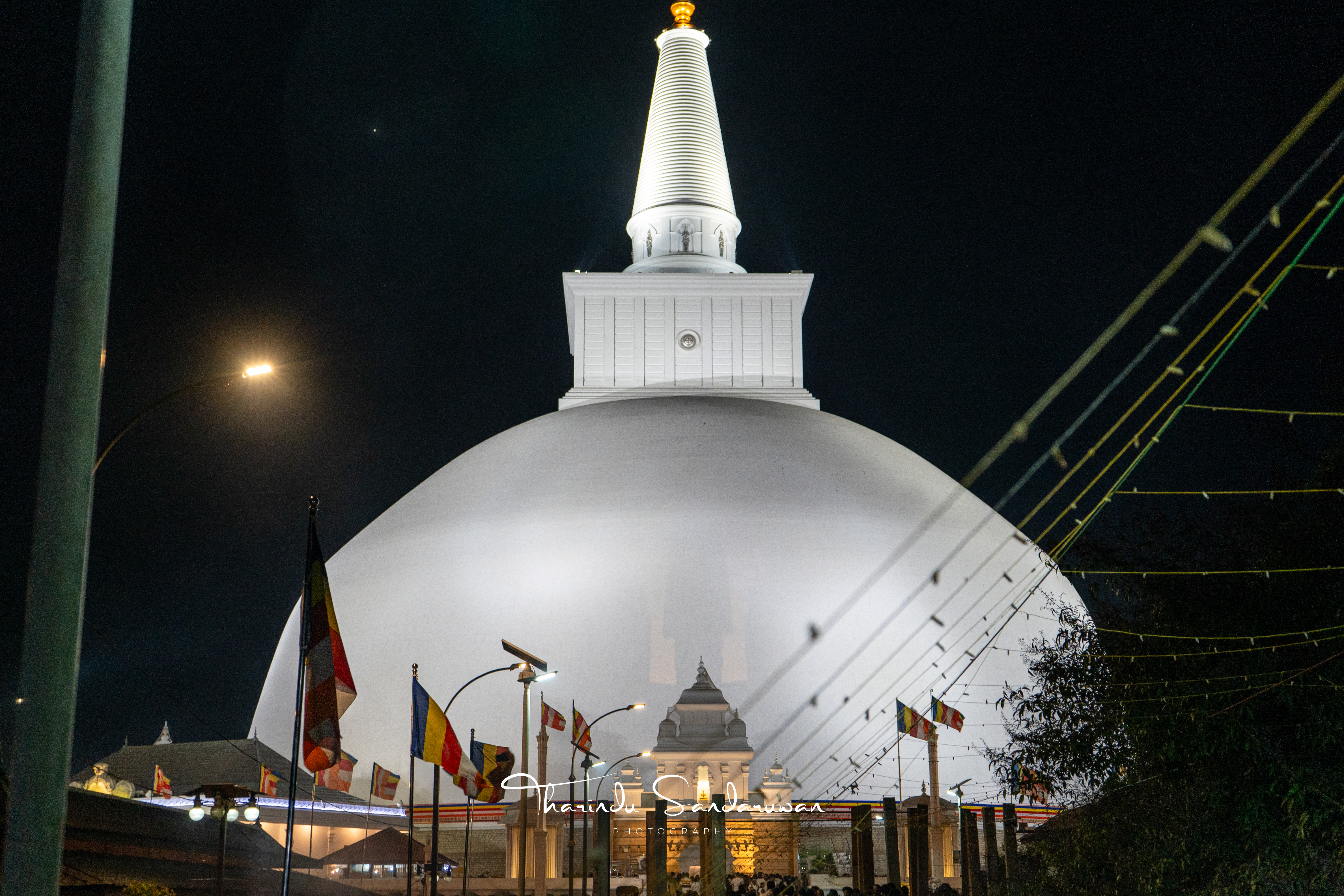 A brightly illuminated white stupa and colourful flags against the night sky.