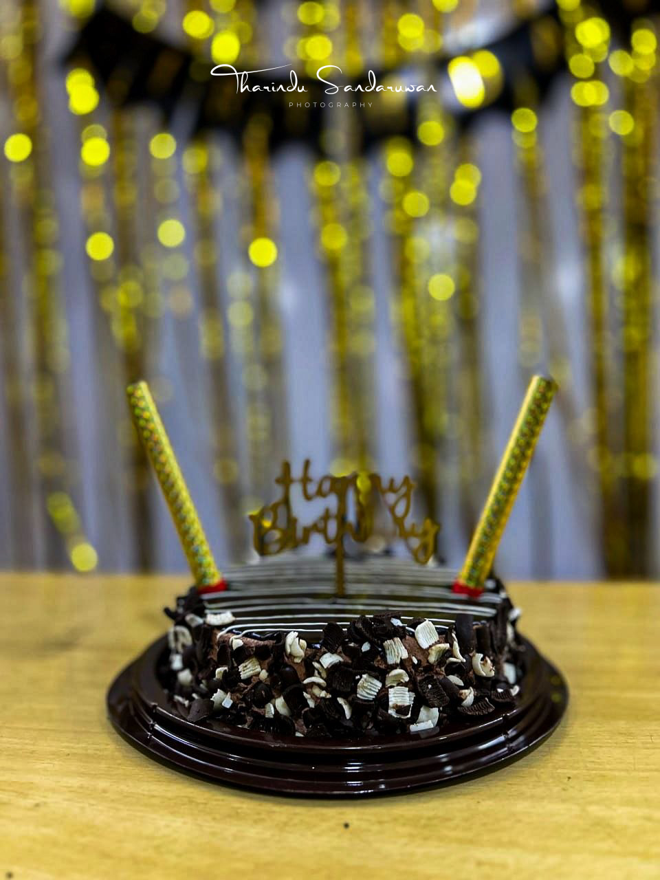A chocolate birthday cake with candles and a gold Happy Birthday topper.