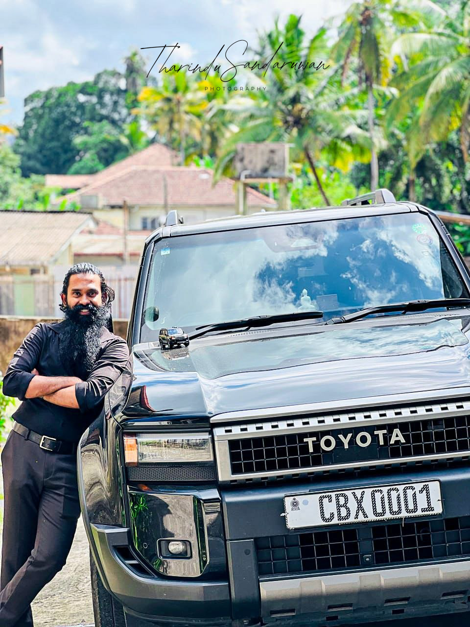A man poses beside a parked vehicle outdoors.