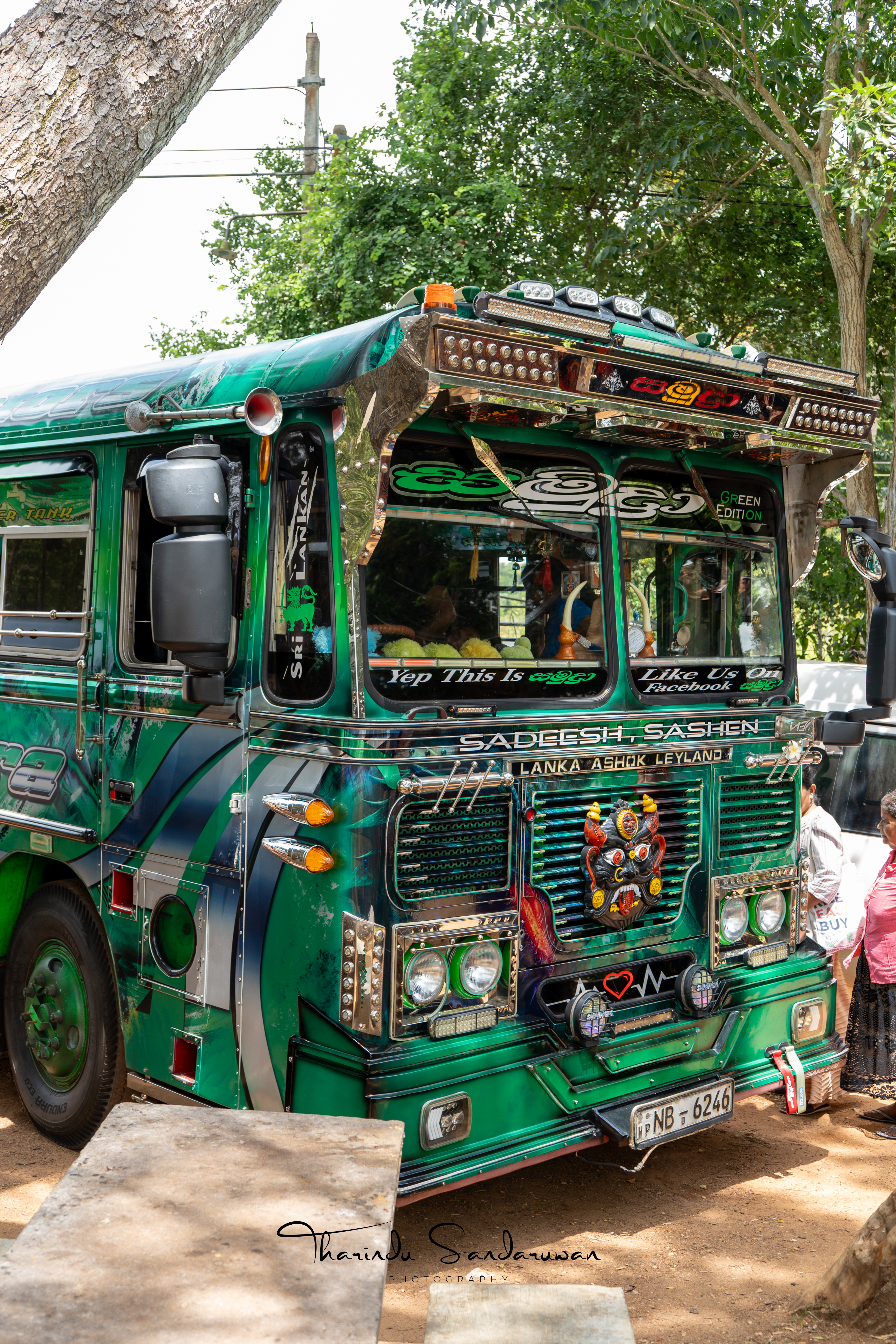 A brightly decorated Sri Lankan bus parked beneath trees.