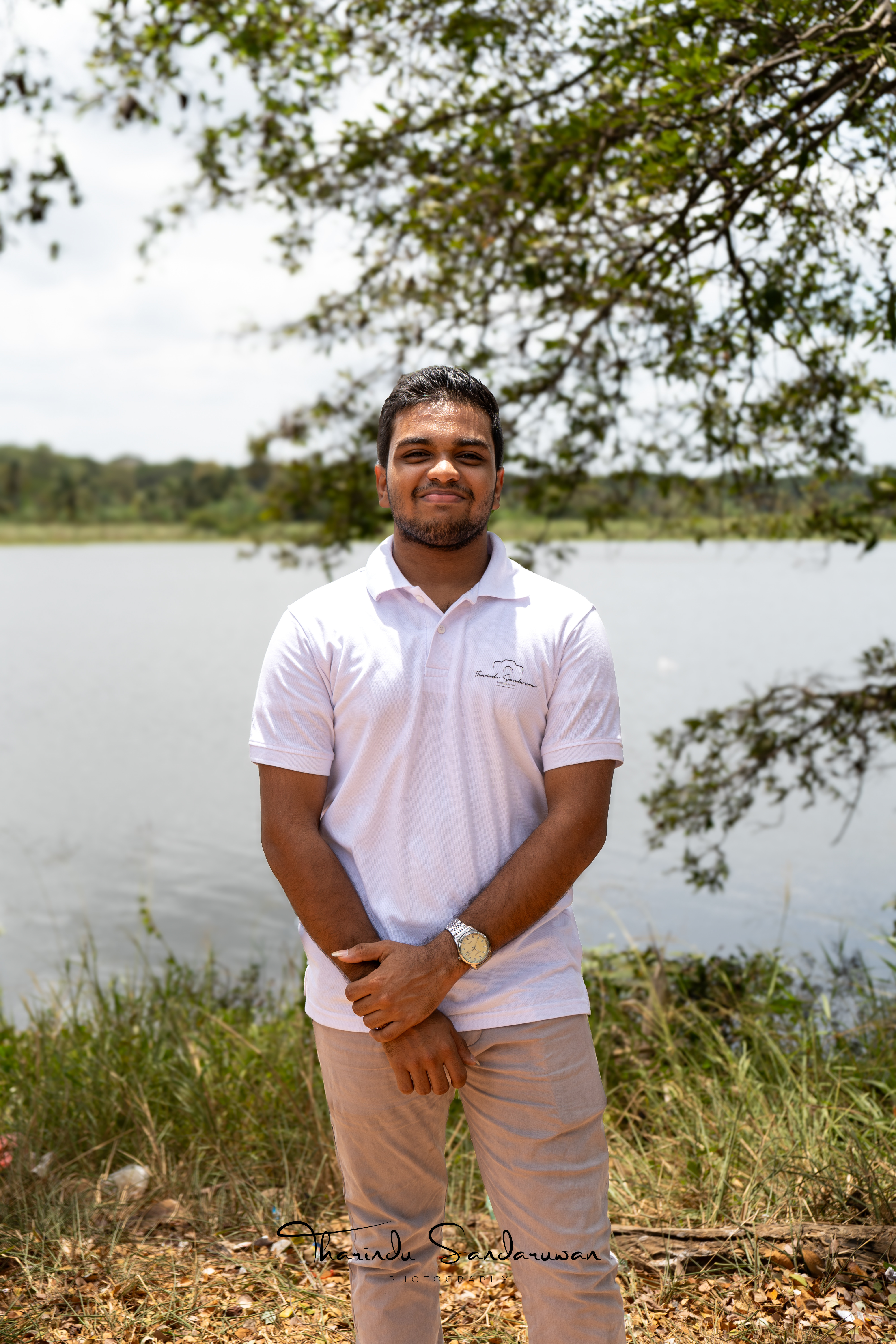 Tharindu Sandaruwan standing beside a lake beneath tree branches.