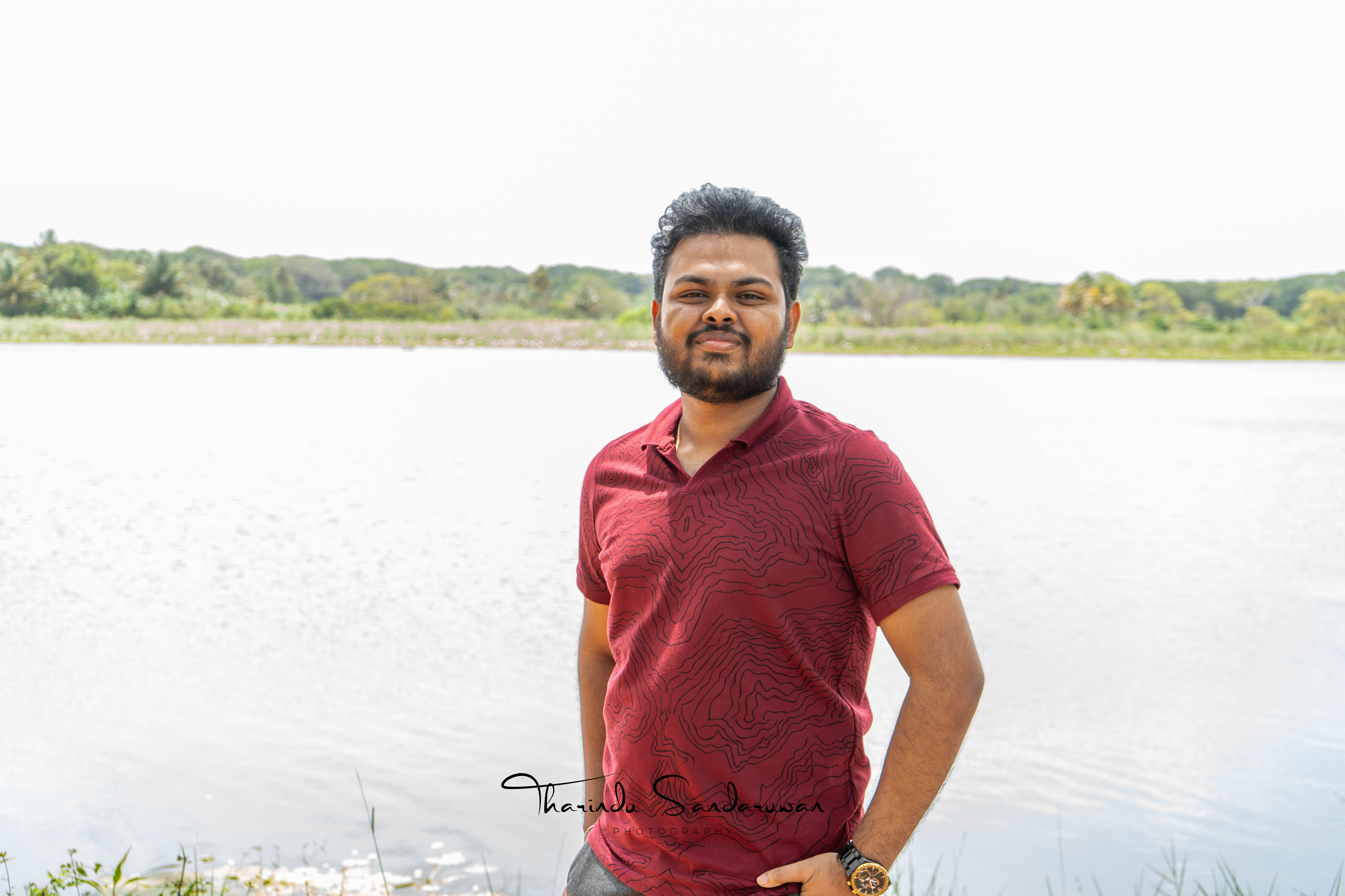 Tharindu Sandaruwan standing beside the water in a red shirt.