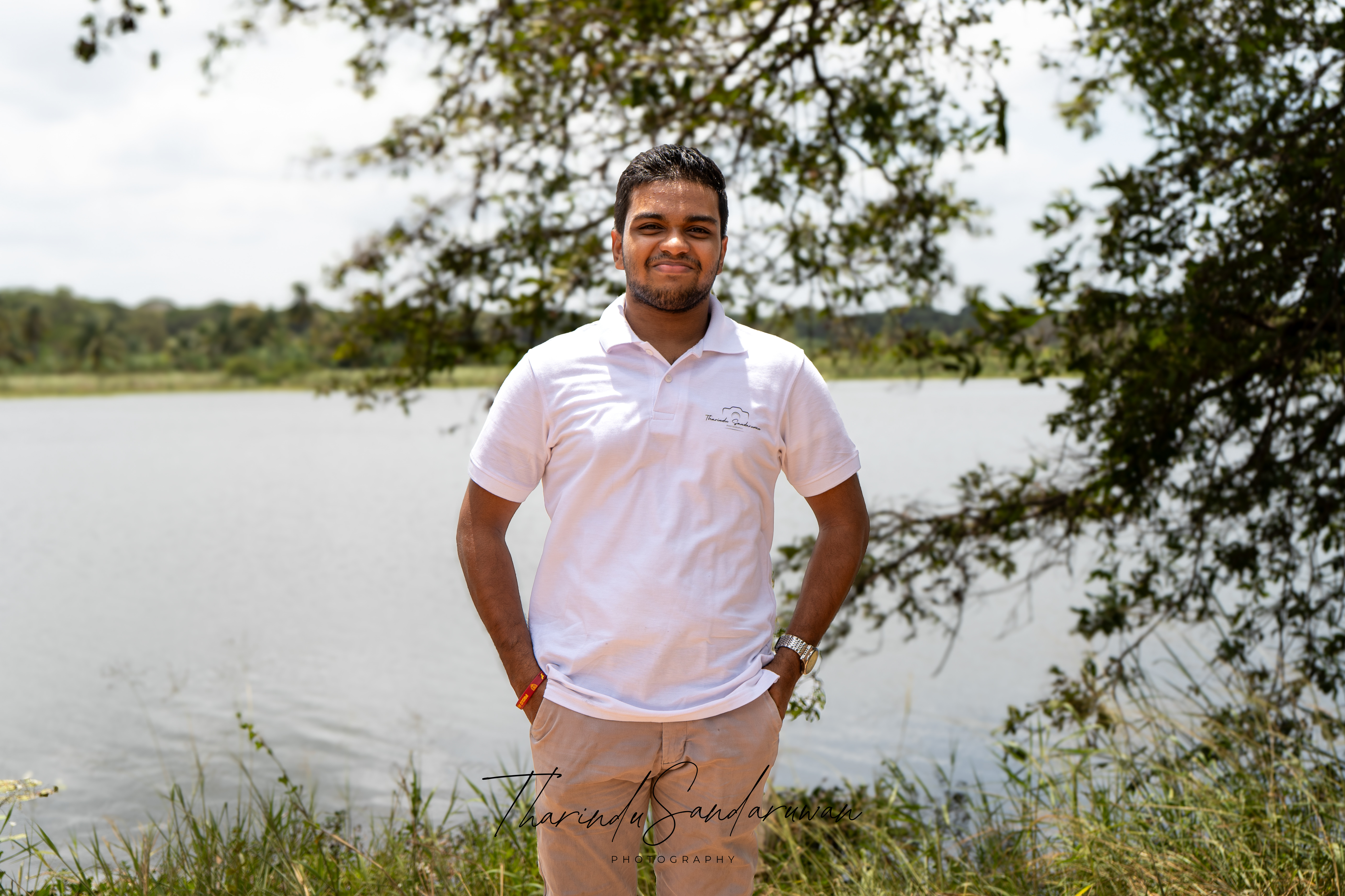 Tharindu Sandaruwan standing by the water beneath tree branches.